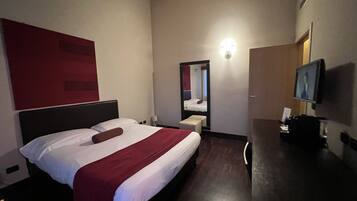 Habitación de hotel con una cama grande, una mesita de noche, un espejo, un televisor y una pared de acento roja.
