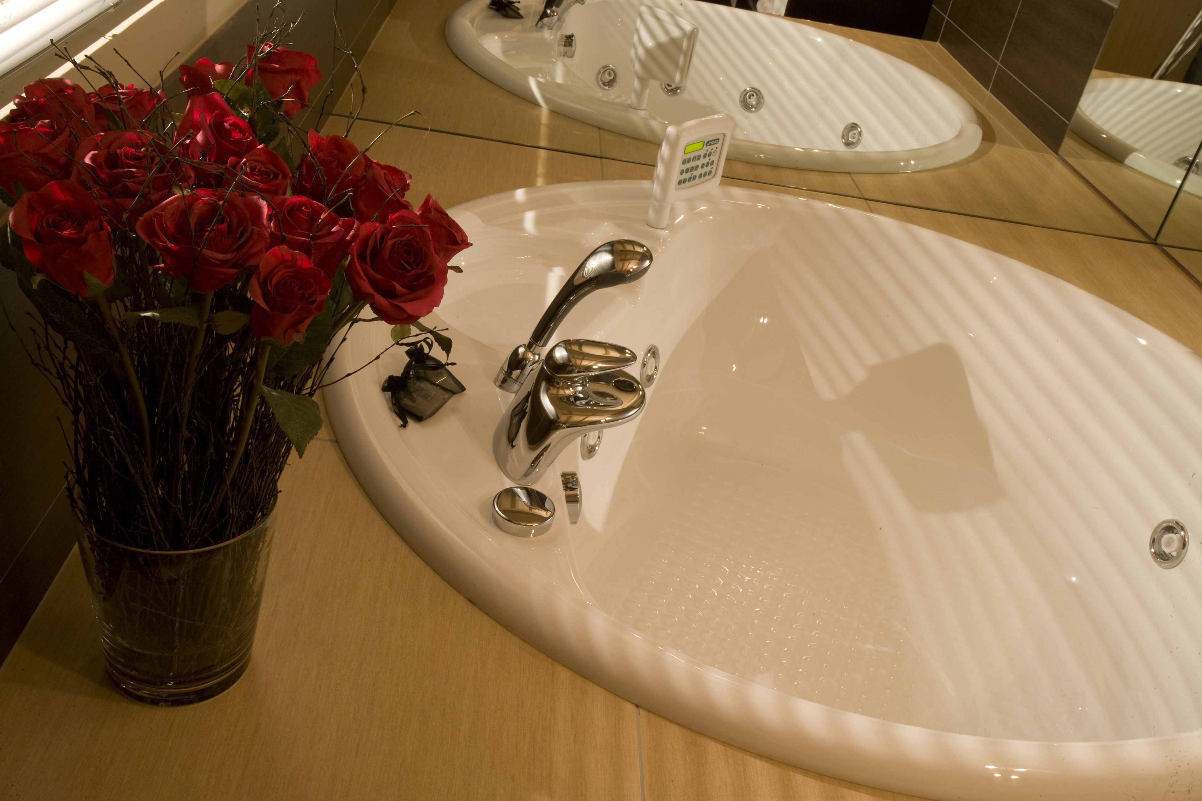 Un baño con un lavabo blanco grande, un espejo y un florero con rosas rojas.