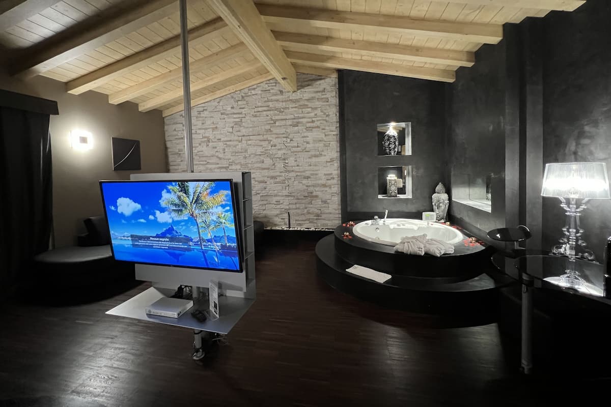 A modern bathroom with a stone wall, a bathtub, a vanity, and a television on a cart.