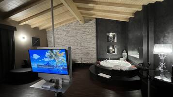 A modern bathroom with a stone wall, a bathtub, a vanity, and a television on a cart.