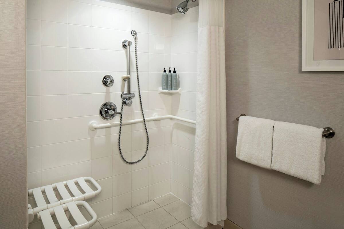 A shower with a handheld showerhead, a handheld shower attachment, and a grab bar.