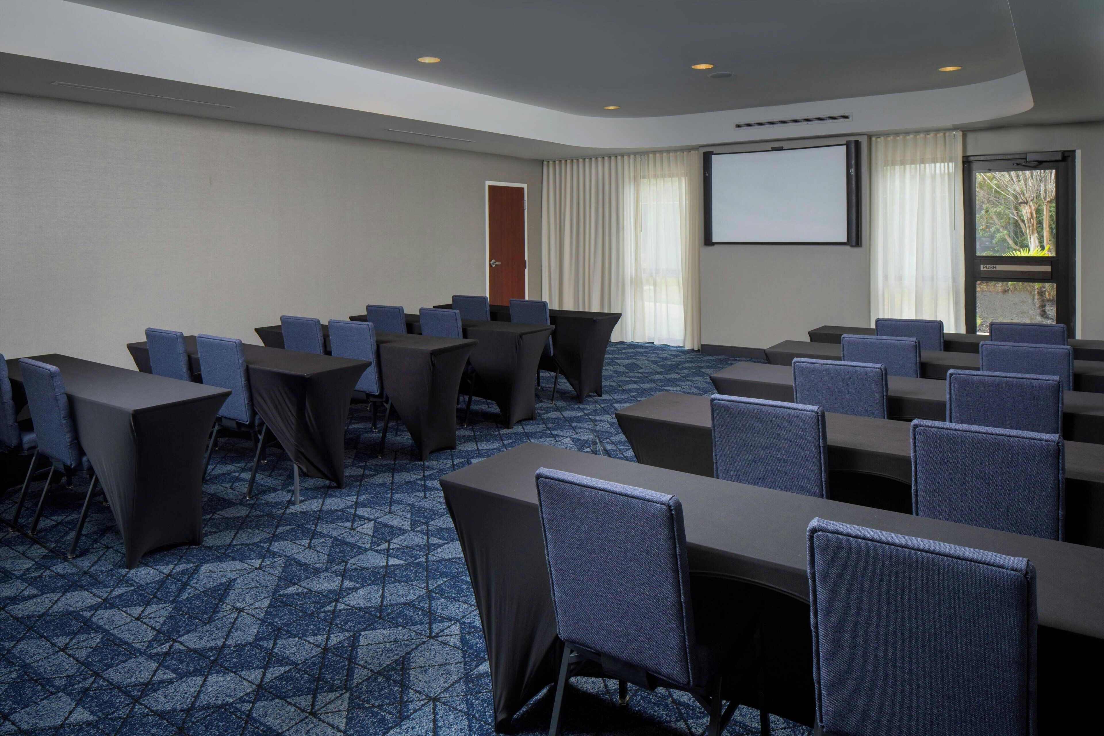 Uma sala de conferências com um grande ecrã, várias mesas e cadeiras dispostas para reuniões.