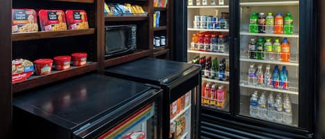 Una kitchenette con microondas, un refrigerador lleno de bebidas y estantes con aperitivos y condimentos.
