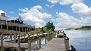 A wooden pier extending into calm water, with a building featuring a green roof and a deck on the left. - Courtyard by Marriott Mobile Daphne/Eastern Shore (Spanish Fort)