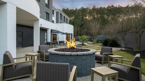 An outdoor seating area with wicker chairs and tables, a circular fire pit, and a building in the background. - Courtyard by Marriott Mobile Daphne/Eastern Shore (Spanish Fort)