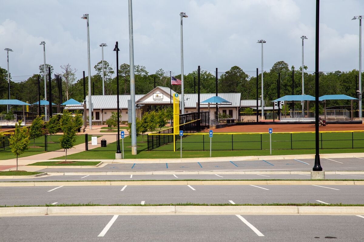 A parking lot with marked spaces, a building with a flag, and a sports field in the background.