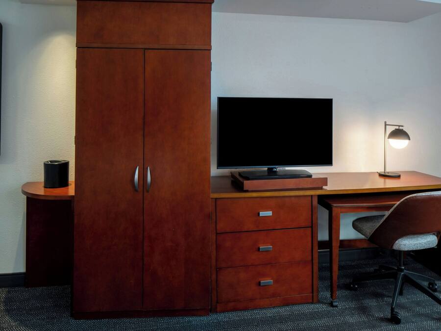 Et træskrivebord med et fladskærms-tv, en lampe og en stol på et hotelværelse.