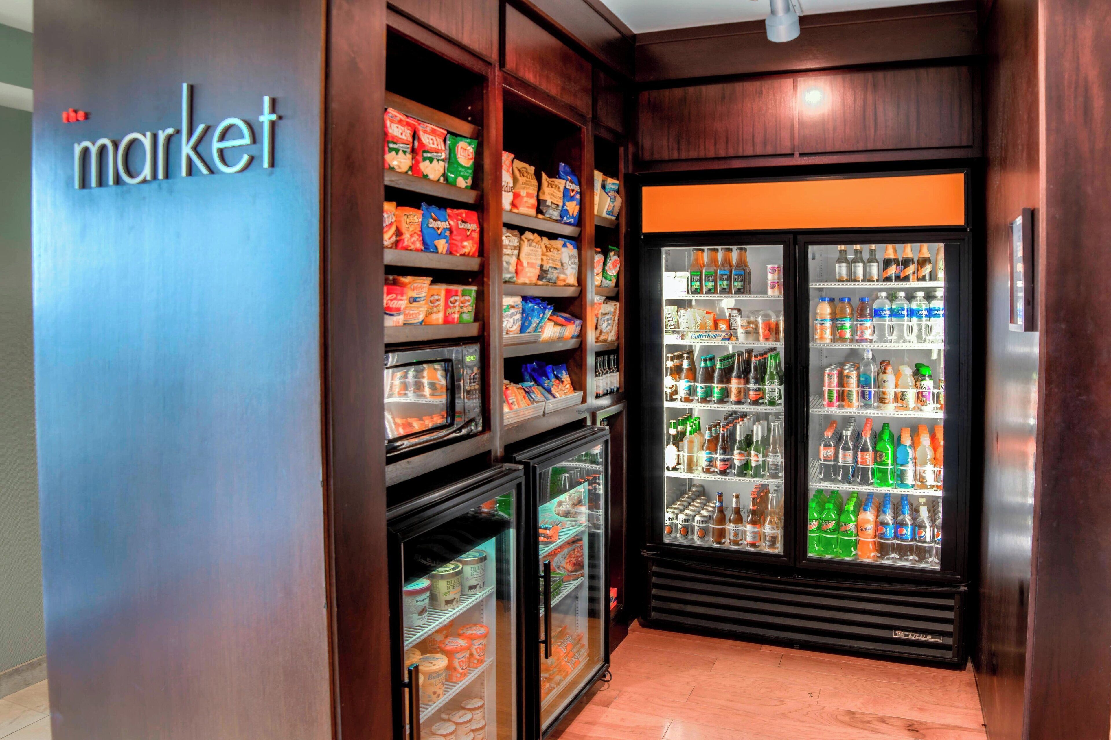 En dagligvarebutik med hylder fyldt med snacks og drikkevarer, samt et køleområde med drikke.