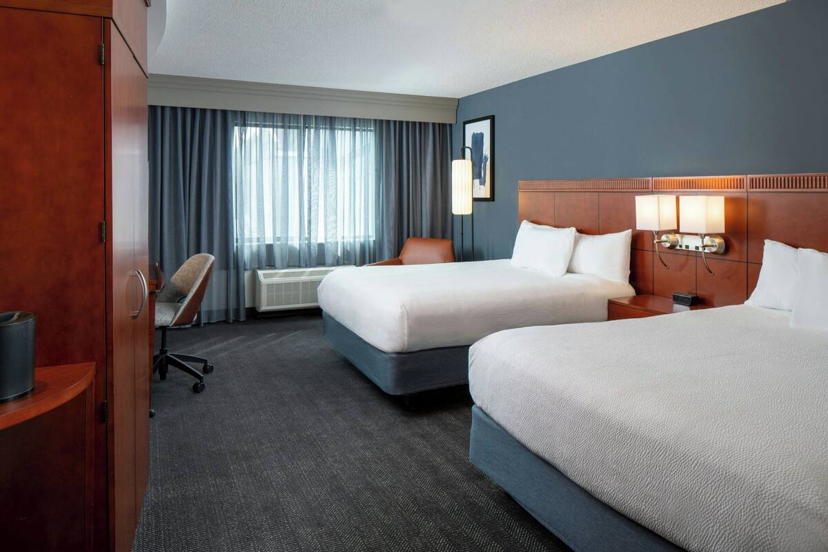A hotel room with two beds, a desk, a chair, a wardrobe, and a window with curtains.