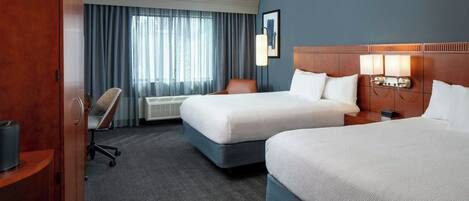 A hotel room with two beds, a desk, a chair, a wardrobe, and a window with curtains.