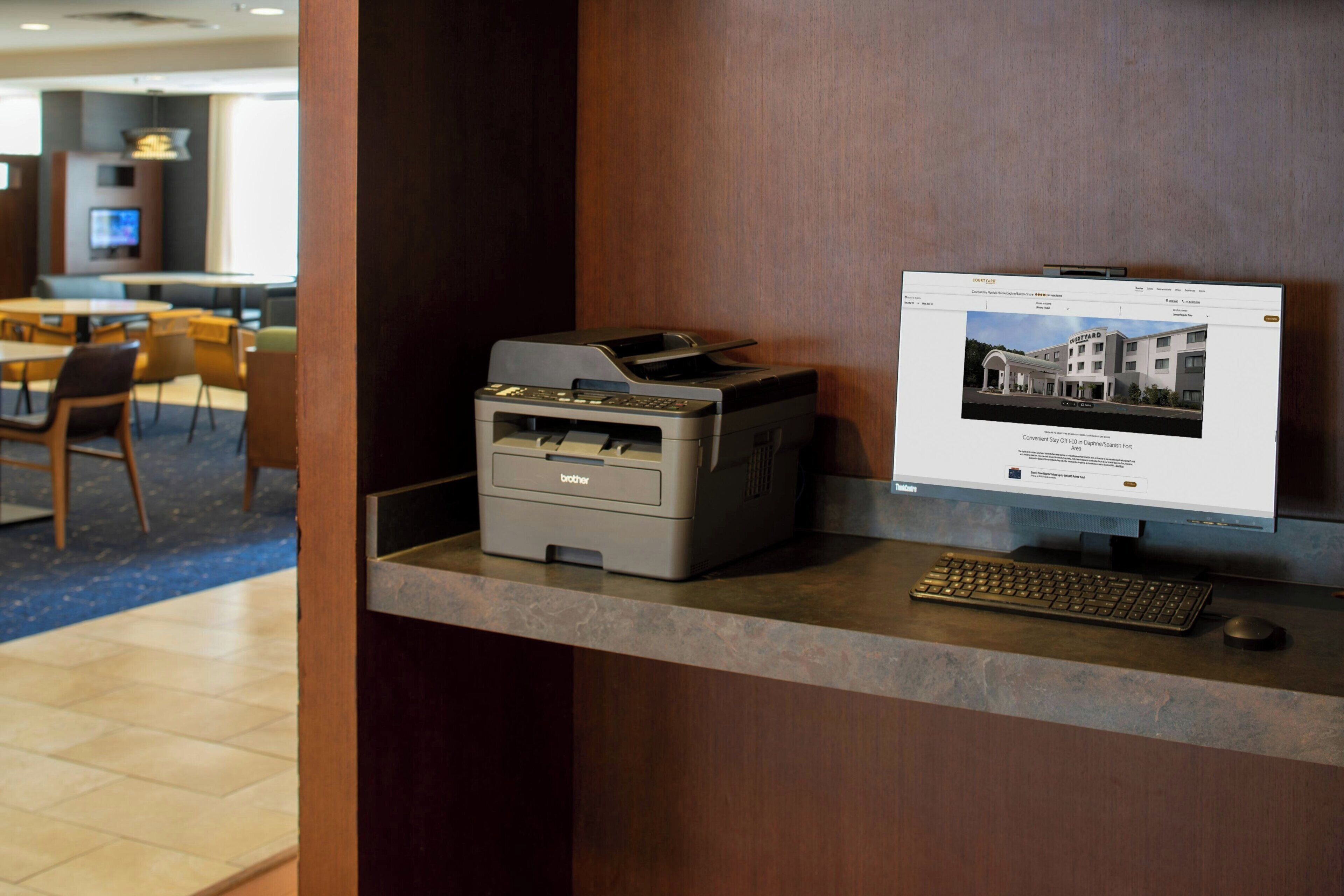 Un mostrador de recepción con una impresora Brother, un monitor de ordenador que muestra una imagen de hotel y un teclado.
