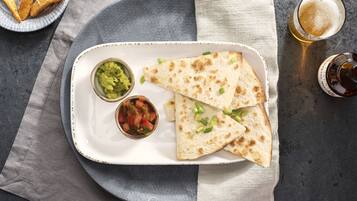 A plate with quesadillas, guacamole, and salsa, accompanied by a glass of beer and a plate of fries.