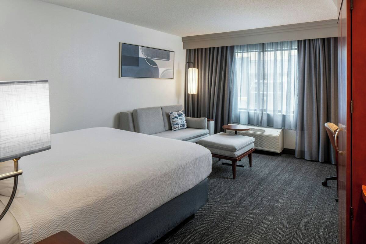 A hotel room with a large bed, a sofa, a small table, and a window with curtains.