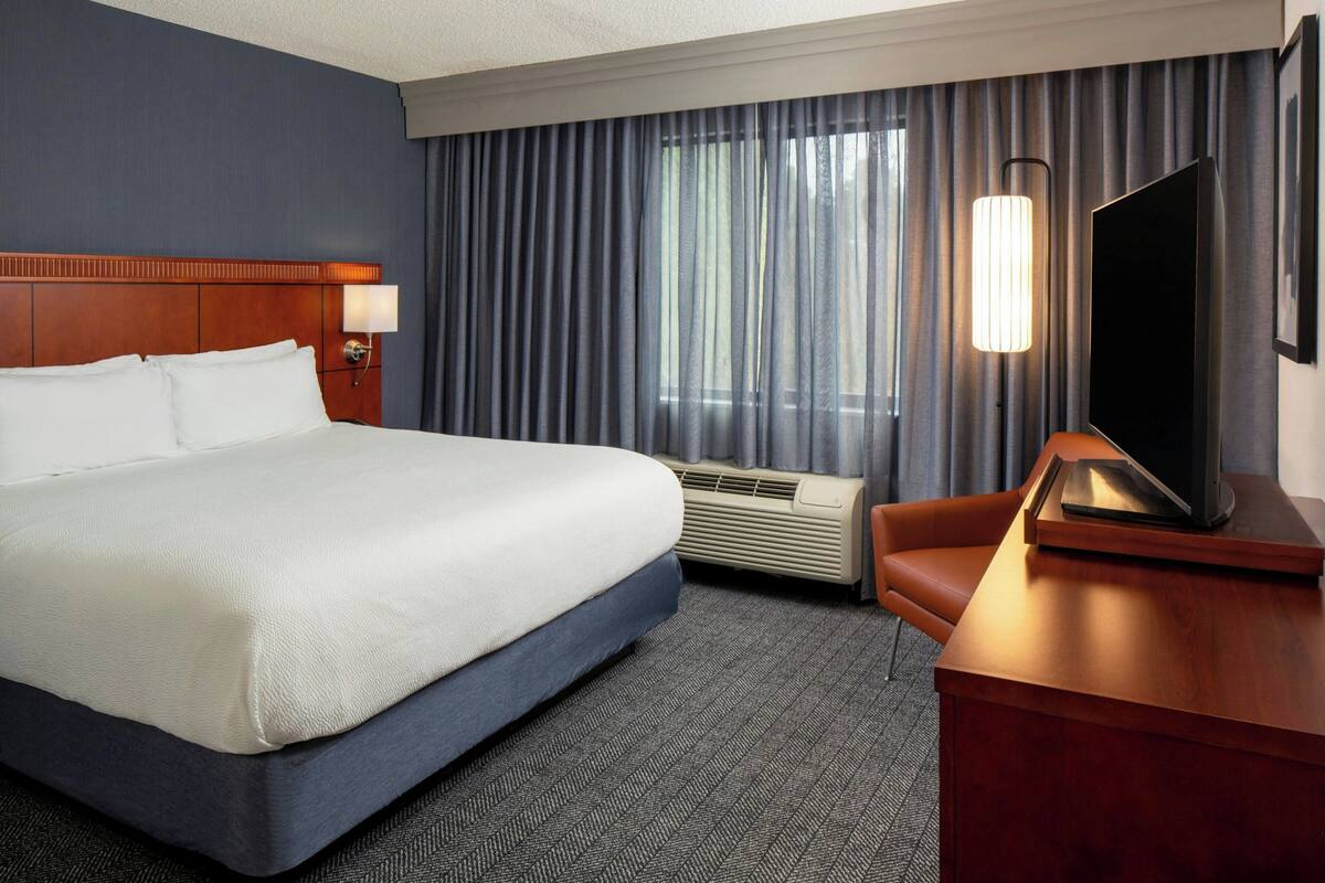 A hotel room with a large bed, a flat-screen TV, a desk, and a window with curtains.