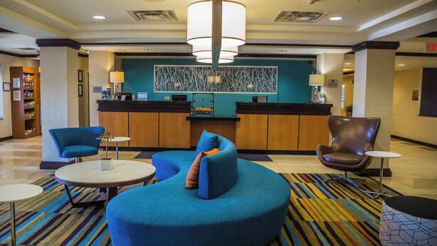 Un vestíbulo con una mesa de recepción, un sofá azul, un sillón marrón y una alfombra estampada.