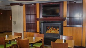 Un hall de hotel con paneles de madera, un televisor de pantalla plana sobre una chimenea, y varias mesas y sillas.