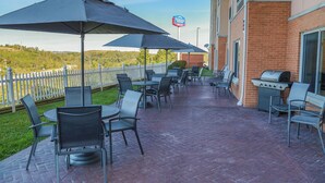 Un patio al aire libre con mesas y sillas, una parrilla y vistas a un paisaje montañoso.