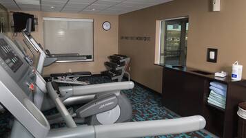 A gym with treadmills, a wall clock, a motivational quote, and a window with a view.