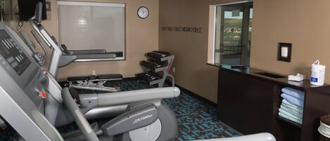 A gym with treadmills, a wall clock, a motivational quote, and a window with a view.