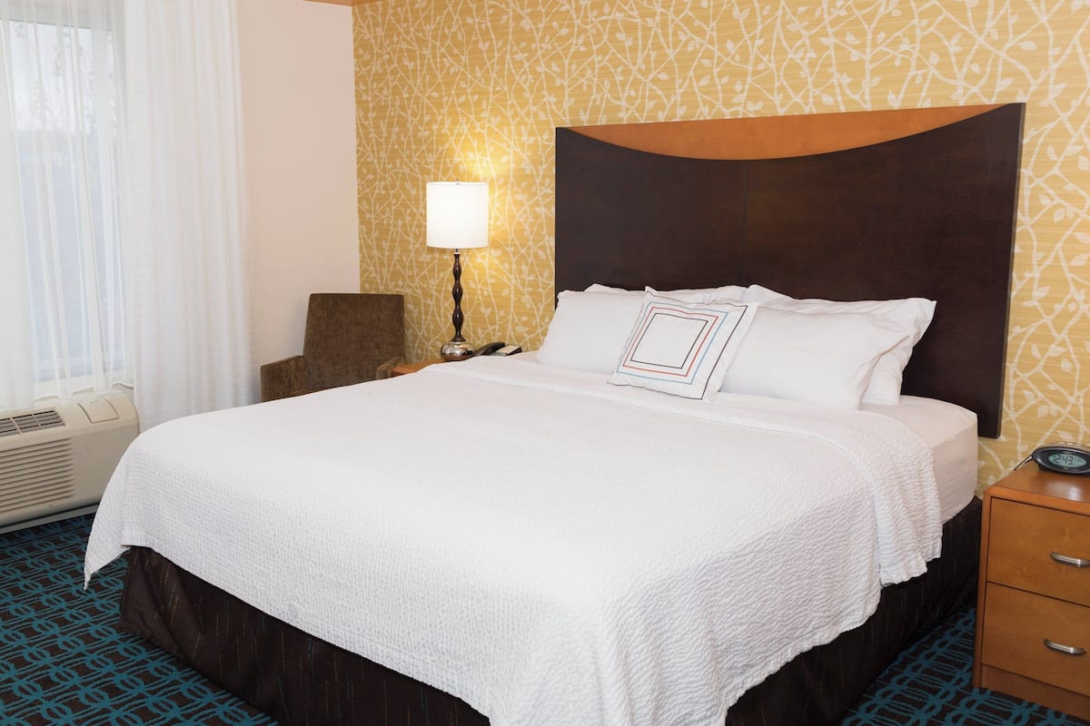 Una habitación de hotel con una cama grande, una mesita de noche con lámpara y un calentador de pared.