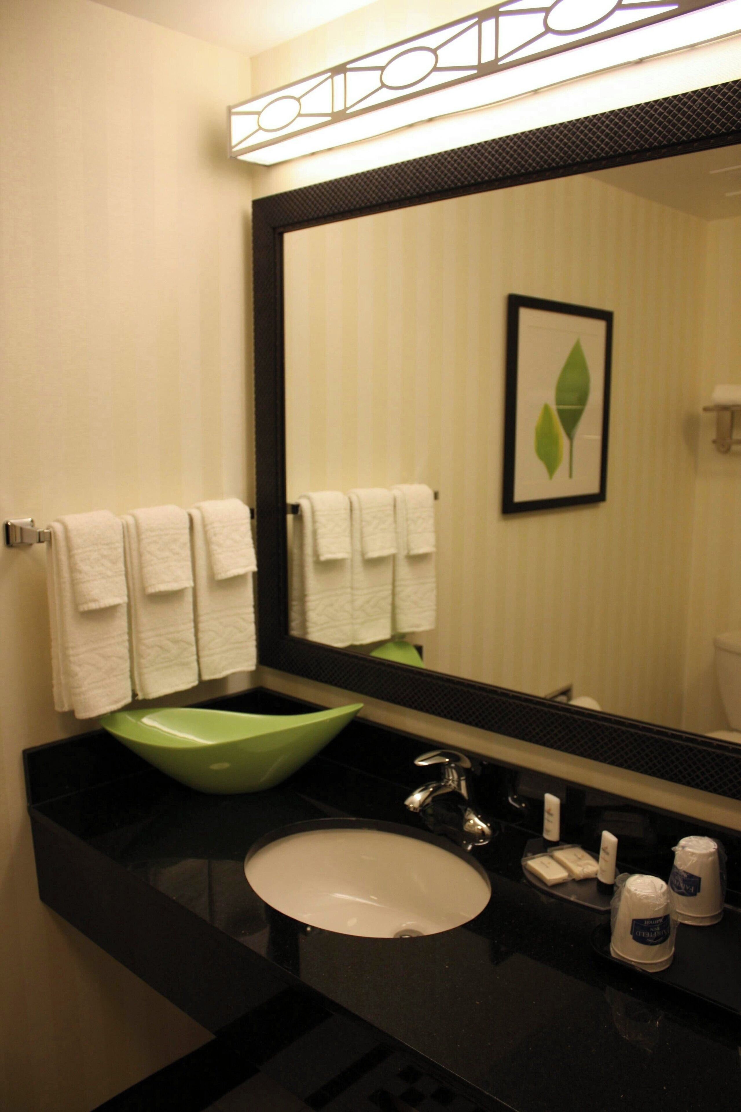 Un baño con un lavabo verde, toallas blancas y un cuadro de una hoja en la pared.