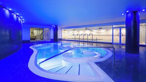 A modern indoor swimming pool with a unique design, surrounded by glass walls and blue lighting. - Radisson RED London Twickenham (Twickenham)
