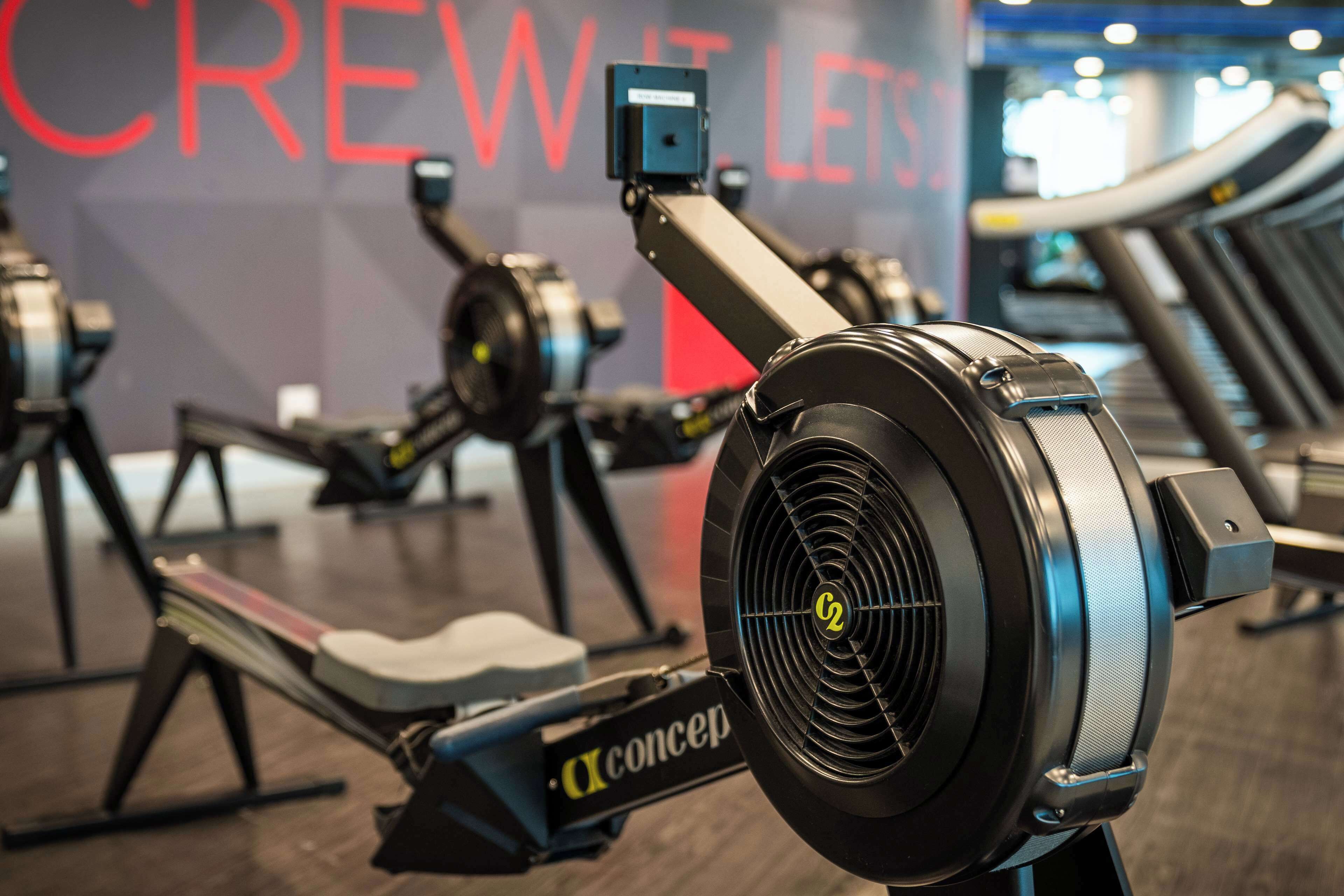 A rowing machine with a digital display and a wall with the text "CREW IT LET'S".