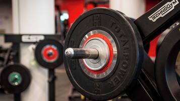 Une barre d’haltérophilie avec des disques de poids rouges et noirs, une barre argentée et une étiquette indiquant « TECHNOGYM ».
