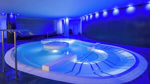 A modern indoor swimming pool with a circular design, surrounded by a tiled deck and a metal railing. - Radisson RED London Twickenham (Twickenham)