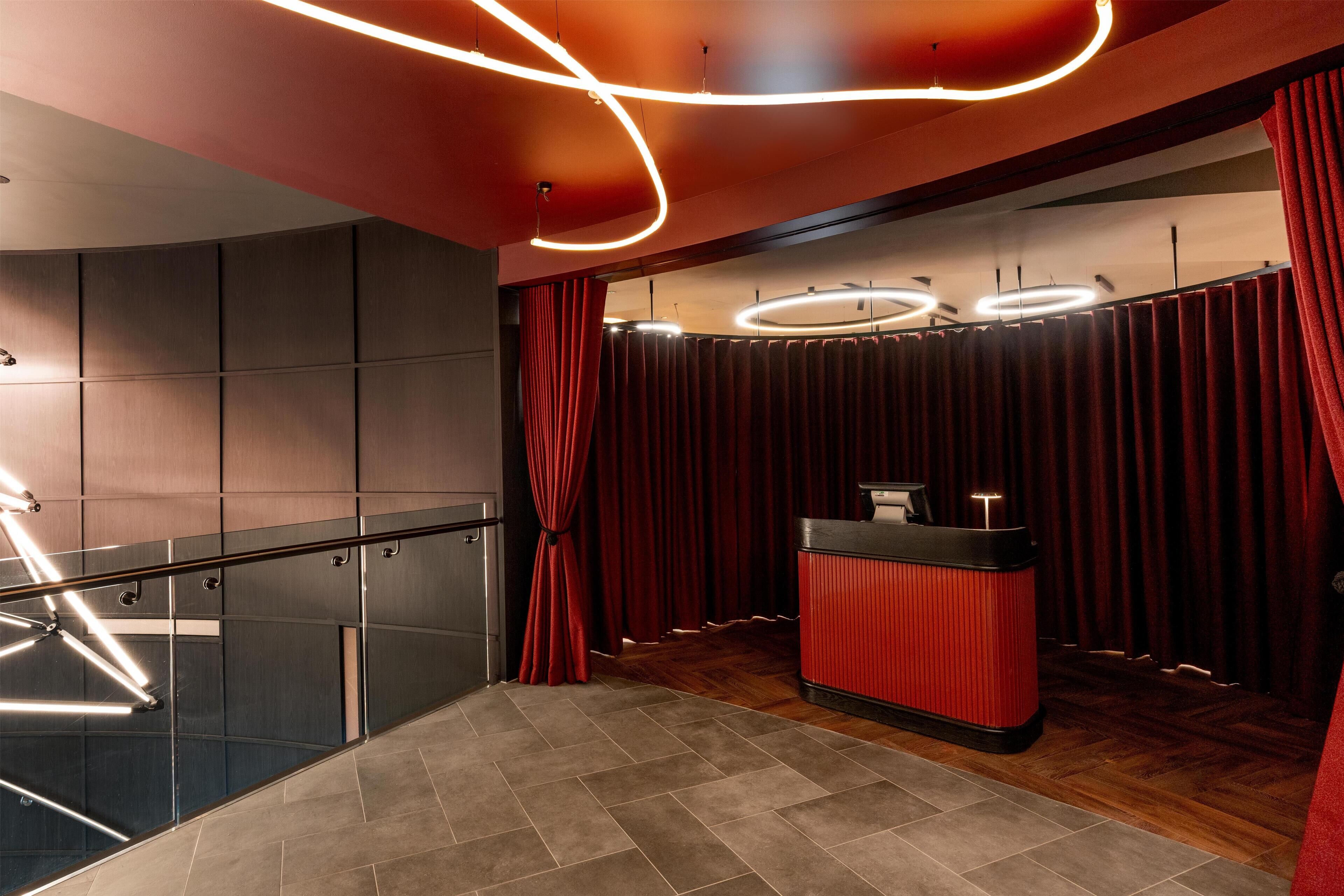A modern interior with a reception desk, red curtains, and a staircase with metal railings.