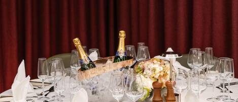 Ein runder Tisch, gedeckt für eine festliche Veranstaltung, mit Mittelstück, Champagnerflaschen und Blumenarrangements.