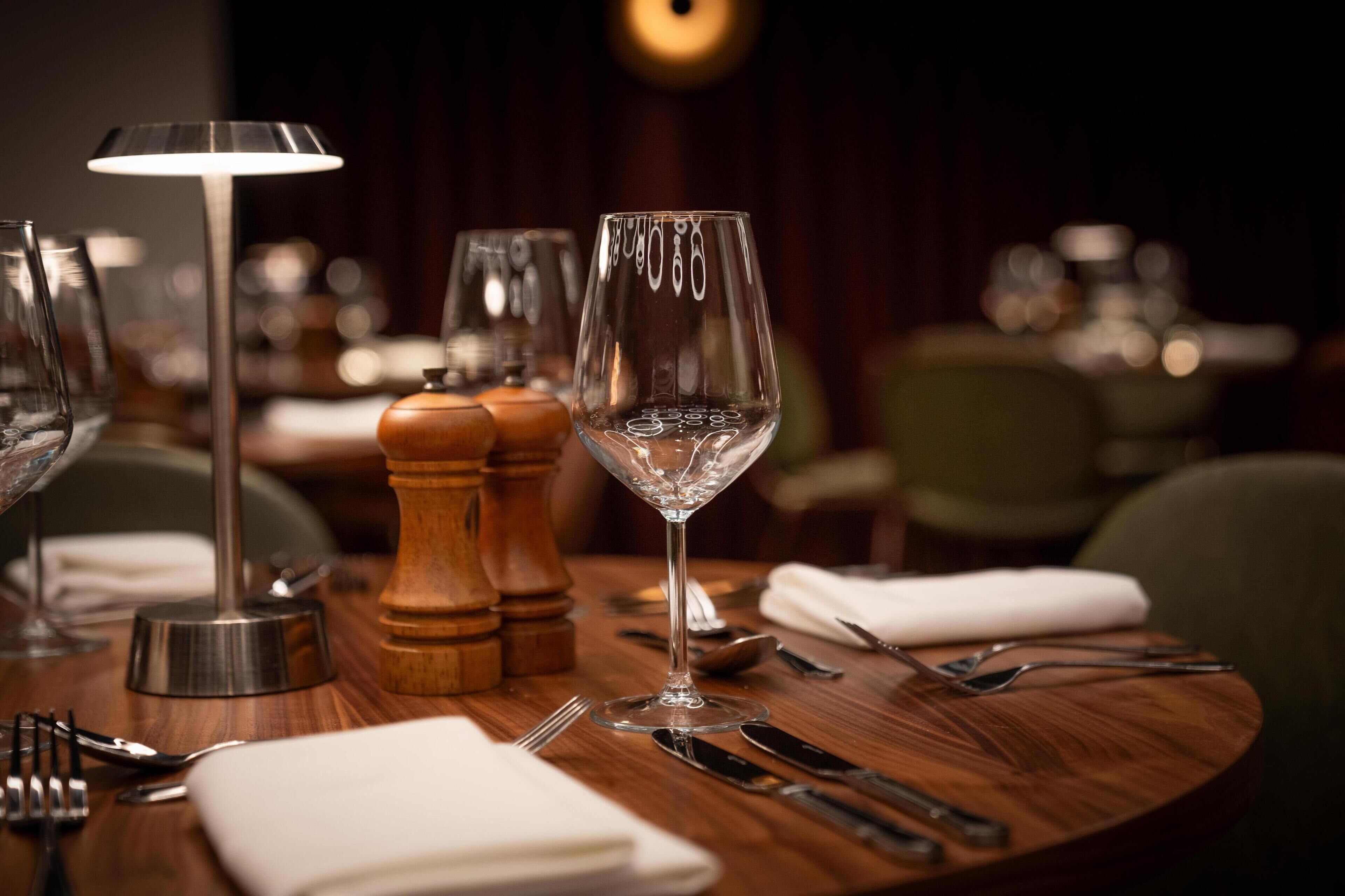 A dining table set with a wine glass, salt and pepper shakers, a lamp, and cutlery.