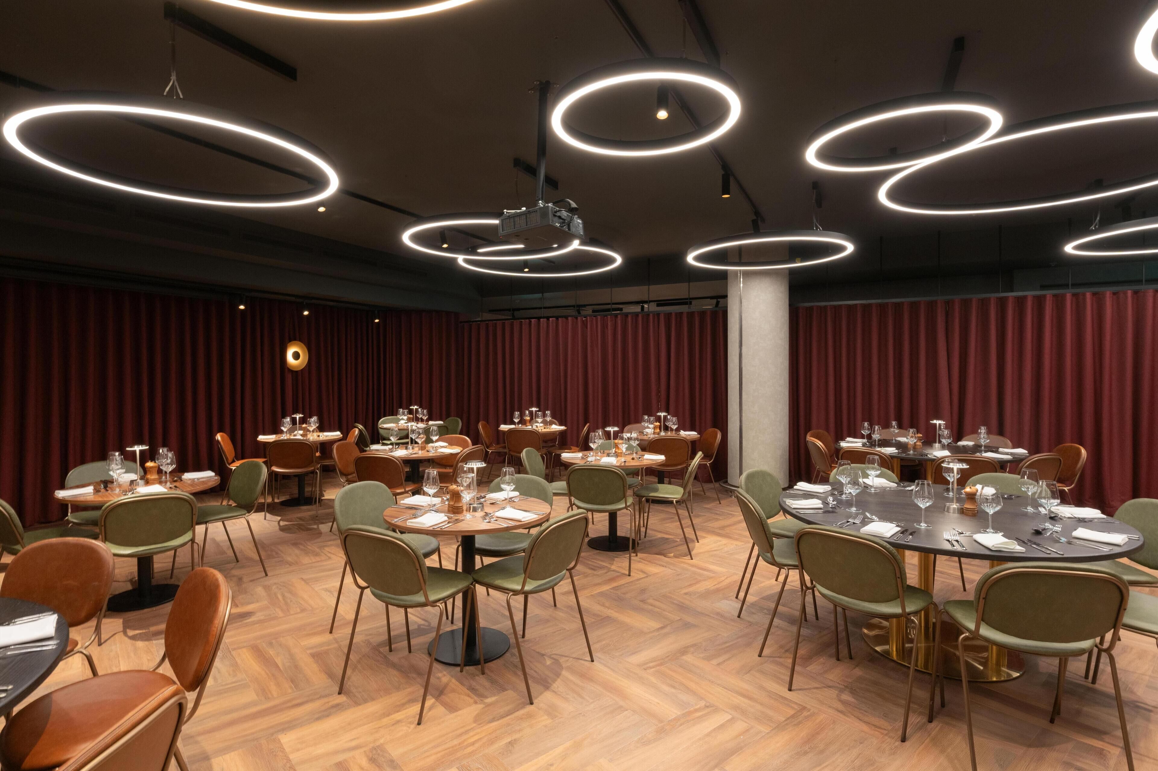 A conference room with round tables and chairs, equipped with projectors and modern lighting fixtures.