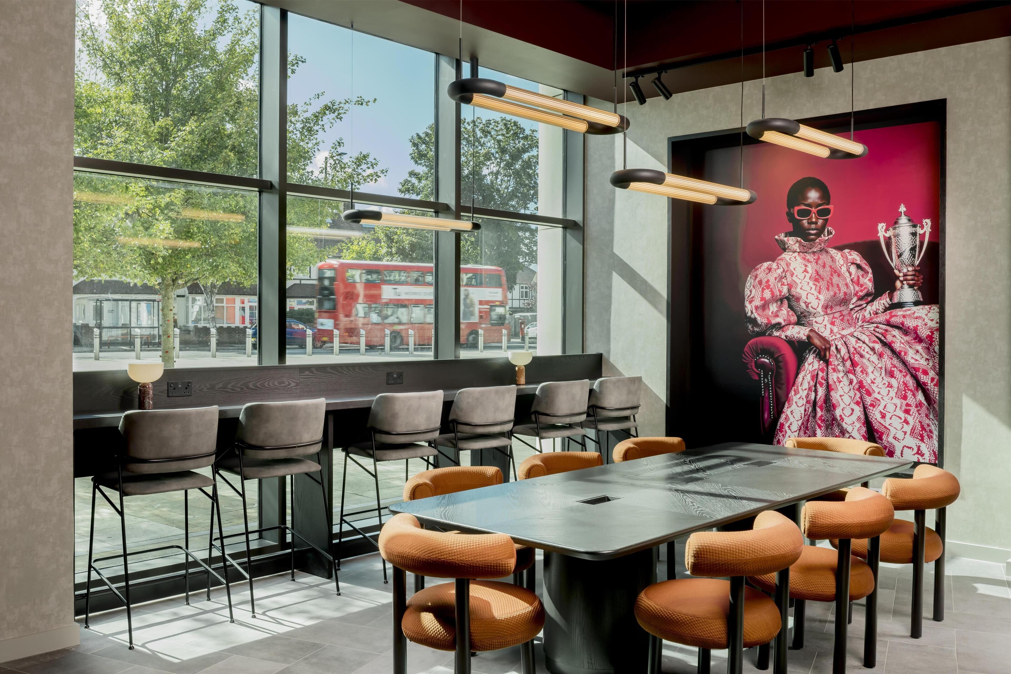 Una sala de conferencias moderna con una gran mesa y sillas, ventanas amplias con vistas a un autobús turístico rojo de dos pisos y un retrato grande en la pared.
