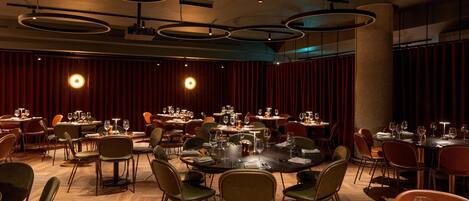 A spacious dining area with multiple tables and chairs, circular ceiling lights, and a wooden floor.