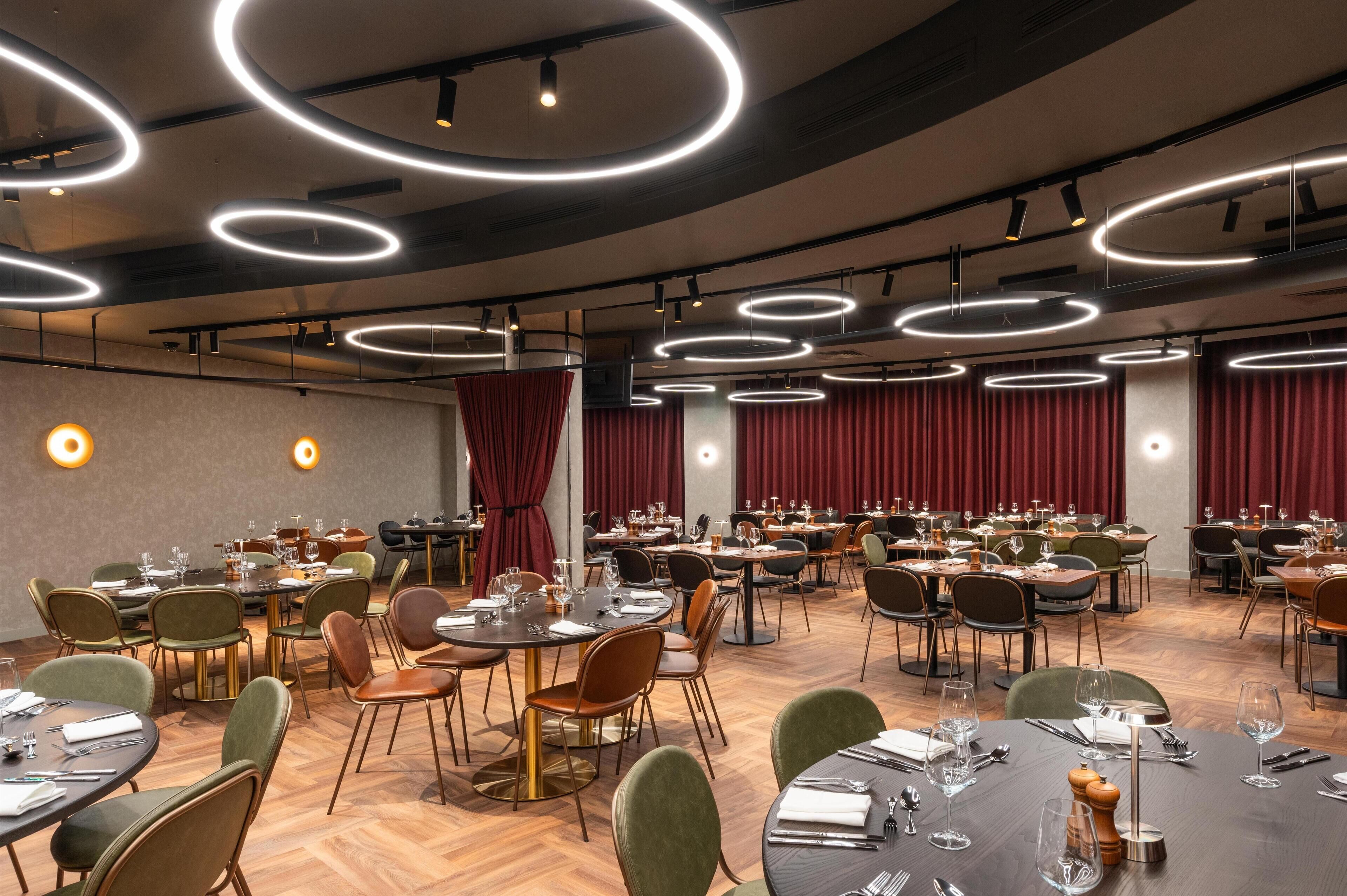A spacious dining area with multiple round tables, chairs, and modern lighting fixtures.