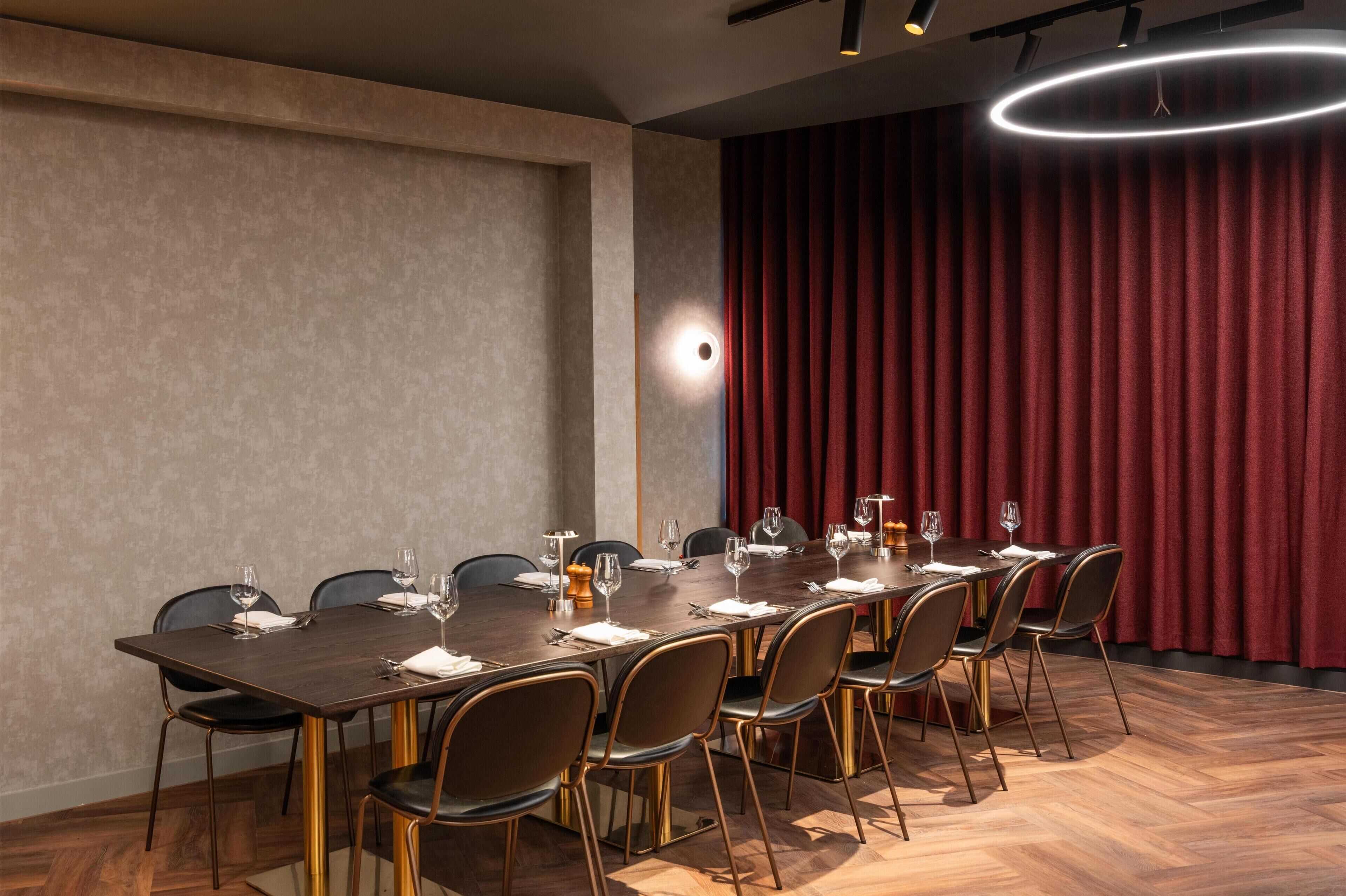 Un salón de conferencias con una larga mesa, sillas y un telón rojo de fondo.