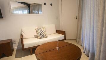 A room with a sofa, a round wooden table, a mirror, and a door with curtains.