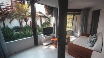 A modern living room with a TV, sofa, and a view of a garden and building outside.