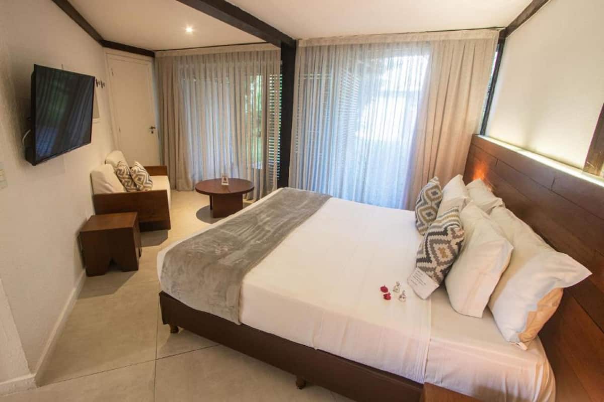 Quarto de hotel com uma cama grande, uma televisão presa à parede, uma mesinha e uma cadeira.
