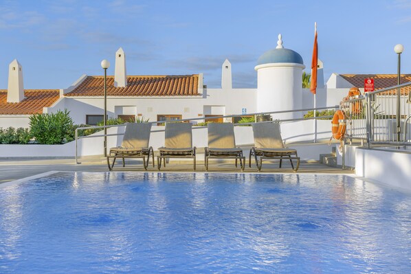 Una piscina con sillas de descanso y vistas a un edificio con cúpula y tejado de azulejos.