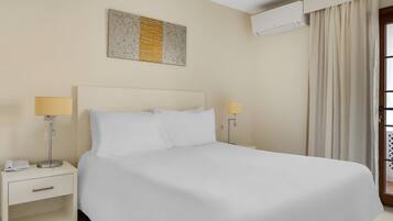 A hotel room with a large bed, two bedside tables with lamps, a wall-mounted air conditioner, and a window with curtains.