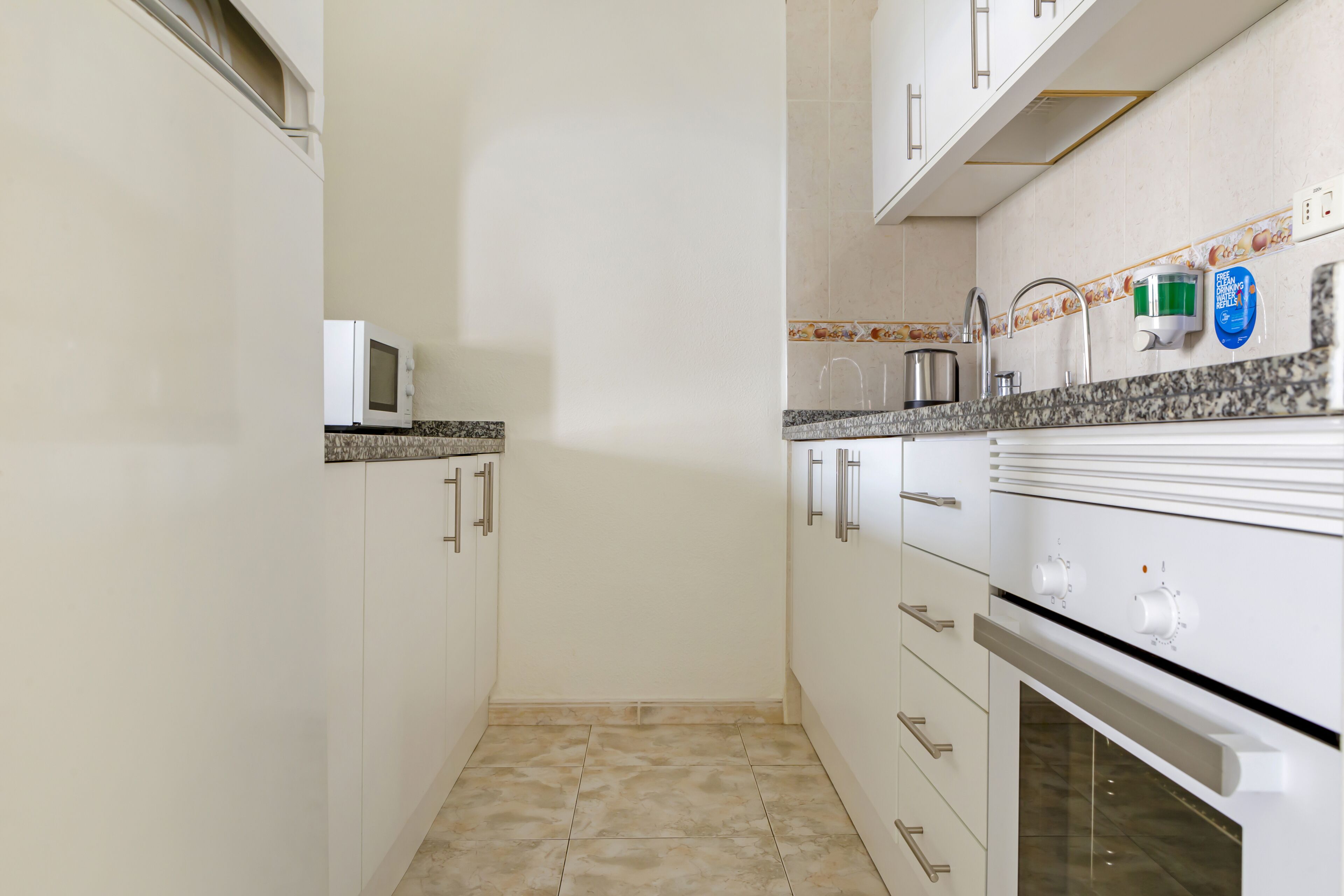 Una cocina compacta con armarios blancos, microondas, lavamanos y estufa.