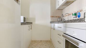 Una cocina compacta con armarios blancos, microondas, lavamanos y estufa.