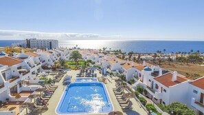 Un resort con piscina central, edificios blancos con techos de tejas rojas y vista al mar.