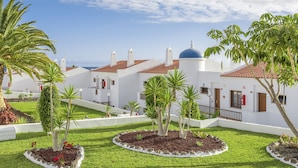 A white building with red-tiled roofs and a blue dome, surrounded by well-maintained gardens and palm trees.