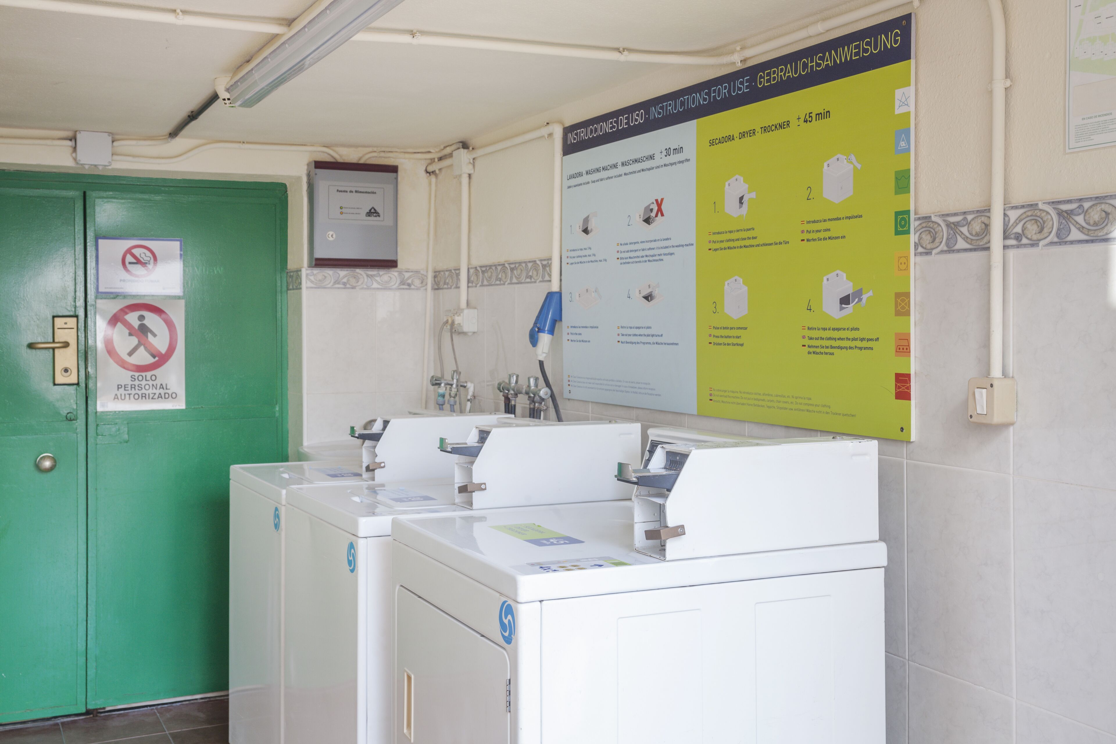 Een wasserette met meerdere wasmachines, een groene deur met een bord en een poster met gebruiksaanwijzingen.