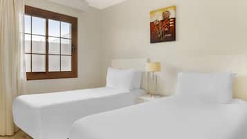 A hotel room with two single beds, a window with curtains, a bedside table with a lamp, and a painting on the wall.