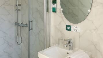 A modern bathroom with a glass-enclosed shower, a white sink with a mirror above it, and a small round mirror on the wall.