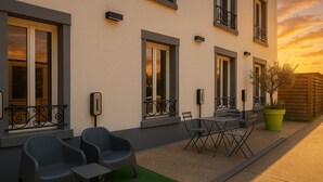 A building with multiple windows, outdoor seating with chairs and a table, and a green artificial turf area. - L'Hôtel du Cirque (Troyes)